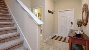 Un escalier recouvert de moquette, une porte blanche, une petite table en bois avec un bol, et un miroir décoratif.