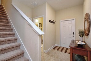 A carpeted staircase, a white door, a small wooden table with a bowl, and a decorative mirror. - Paradise Palms | Private Splash Pool & BBQ | 2 King Beds | Dog Friendly | Near Disney (Kissimmee)