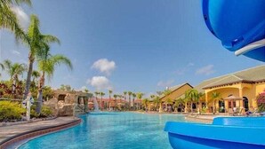 Une piscine avec un toboggan, des palmiers et des bâtiments d’un complexe hôtelier en arrière-plan.