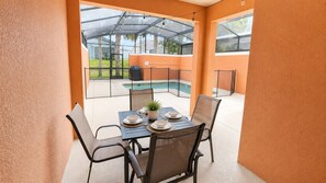 Une terrasse fermée par des baies vitrées, avec une table dressée pour les repas, des chaises et une vue sur une piscine.