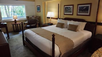 A large bed with a wooden frame, a bedside table, a chair, a lamp, and framed pictures on the wall.