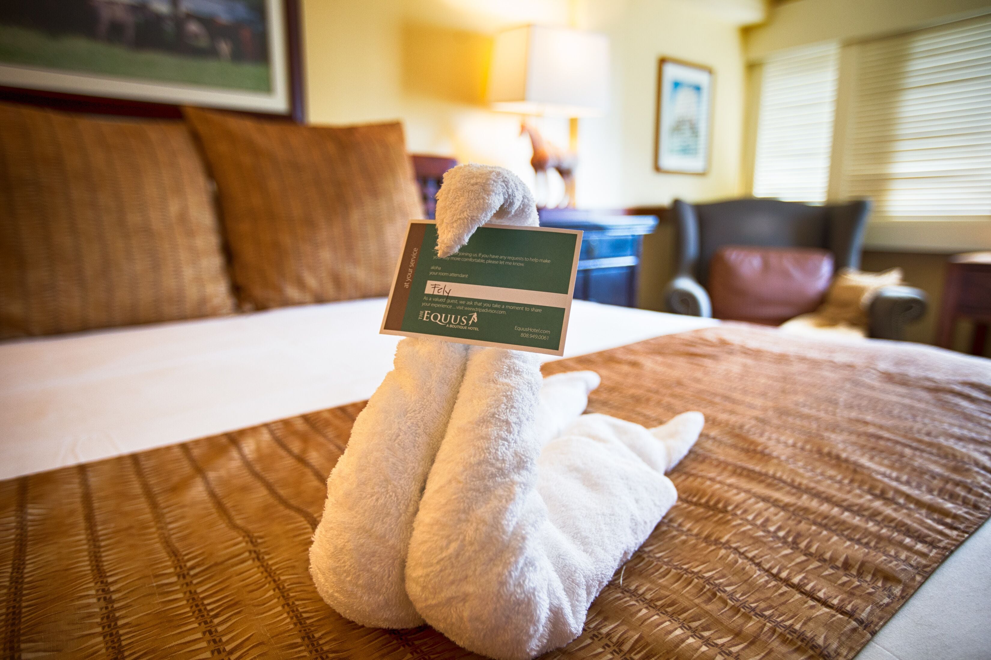 Una cama bien hecha con un portavelas con forma de cisne sosteniendo una tarjeta de presentación.