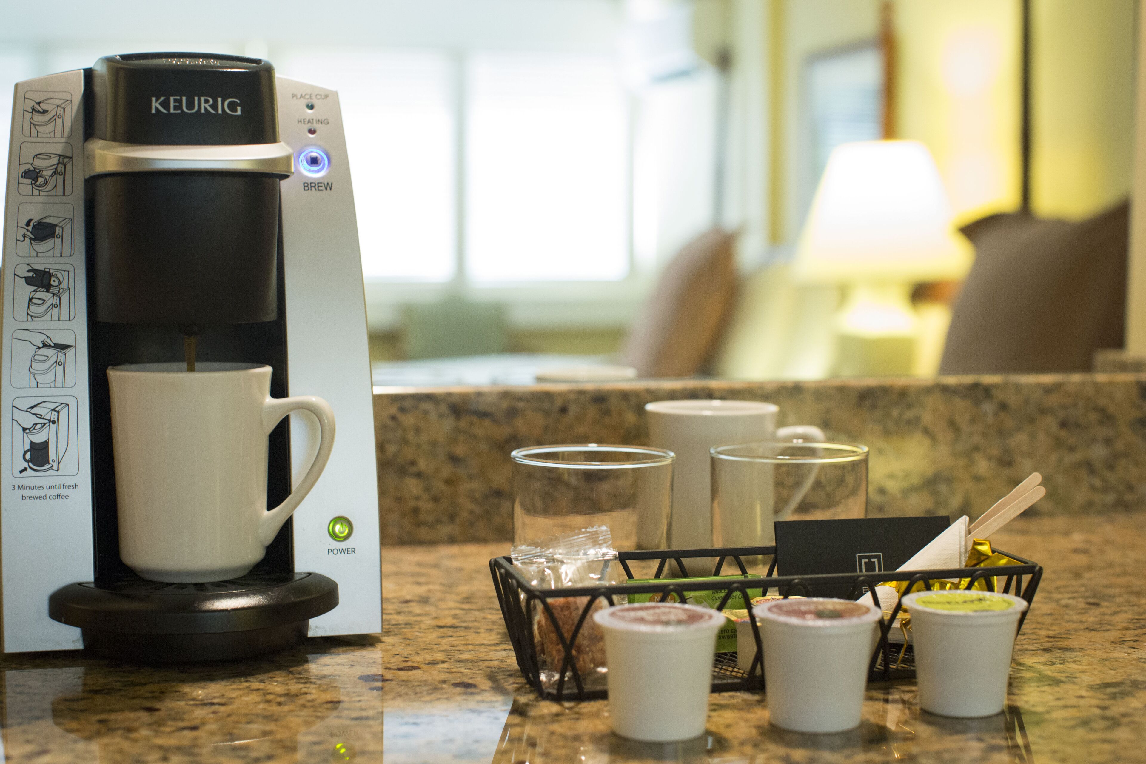 A Keurig coffee maker with a white mug, a glass carafe, and a coffee pod holder on a kitchen counter.