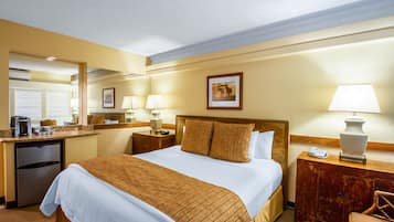 Una habitación de hotel con cama, escritorio con refrigerador, espejo y lámpara.