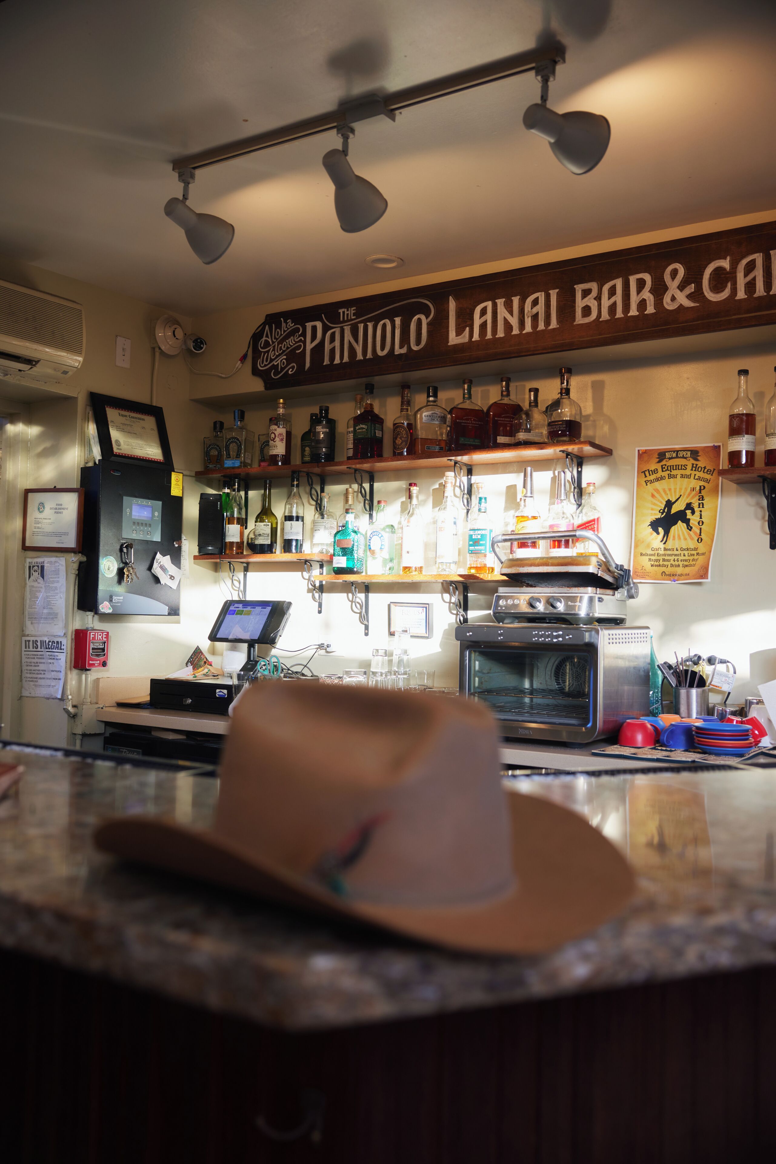 A bar area with a sign reading 'The Panjolo Lanai Bar & Cafe,' a cash register, a digital screen, and a pizza oven.