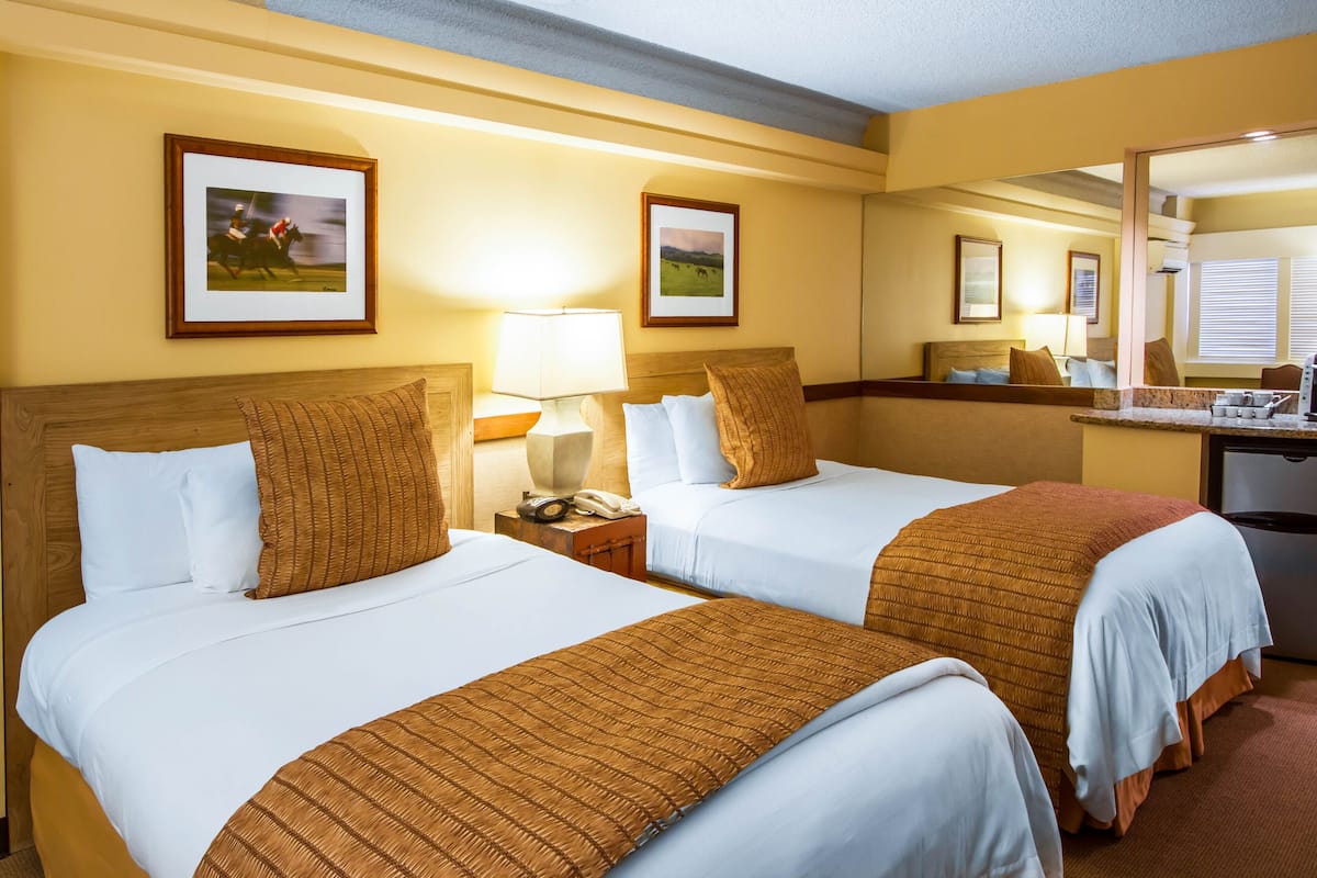 A hotel room with two beds, a nightstand with a lamp, a mirror, and framed pictures on the wall.