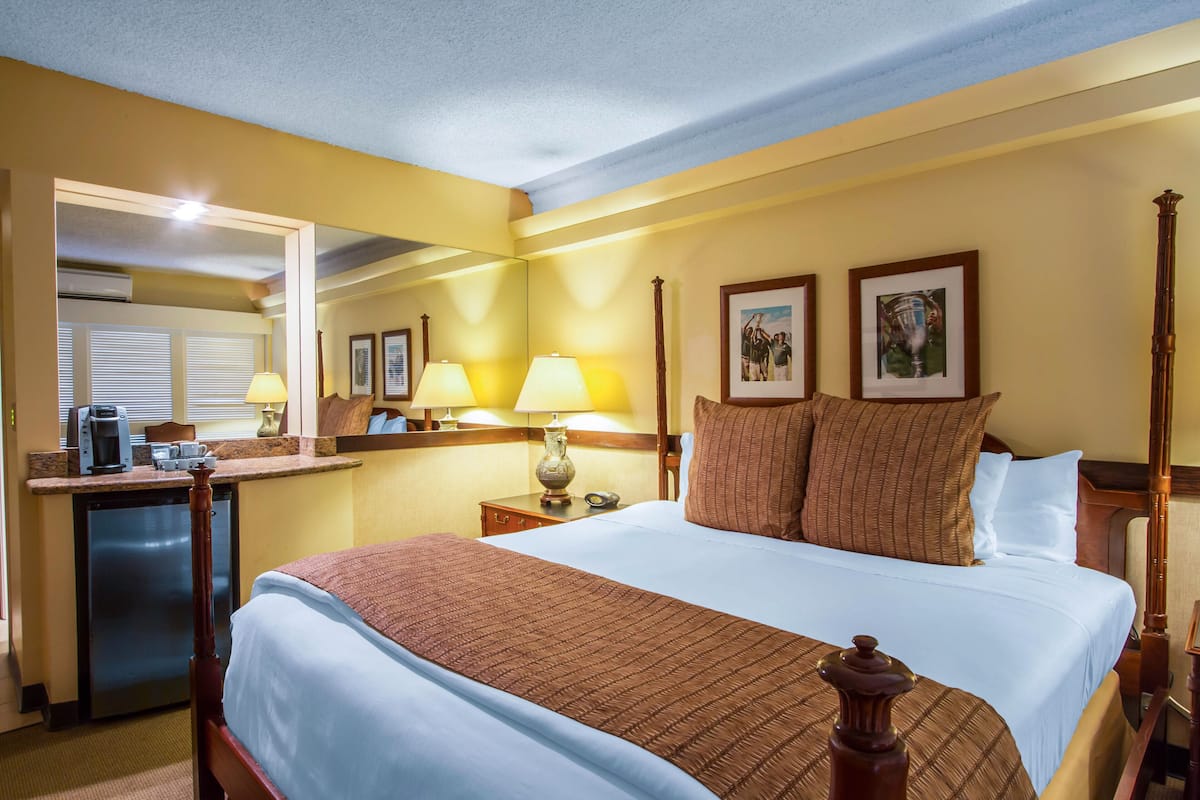 A hotel room with a bed, bedside lamps, a desk with a coffee maker, and a mirror.