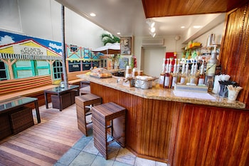 A hotel room with a red sofa, wooden stools, a small table, a mirror, and a kitchen area with wooden cabinets and a countertop. at The Equus