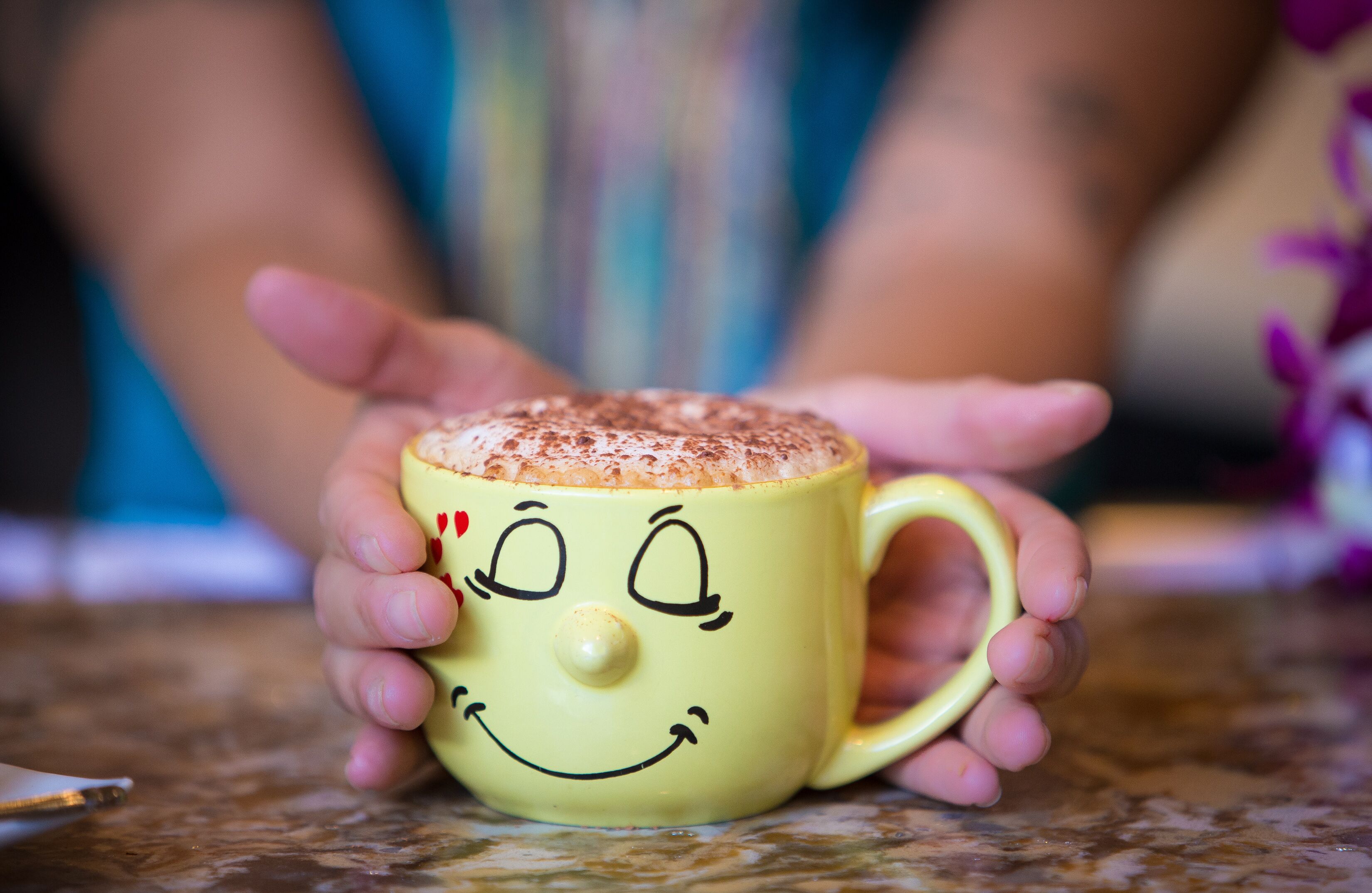 A yellow mug with a smiling face design, held by a person.
