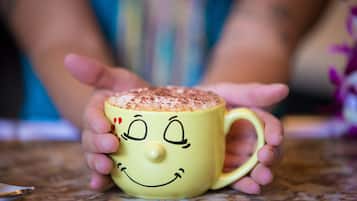 A yellow mug with a smiling face design, held by a person.