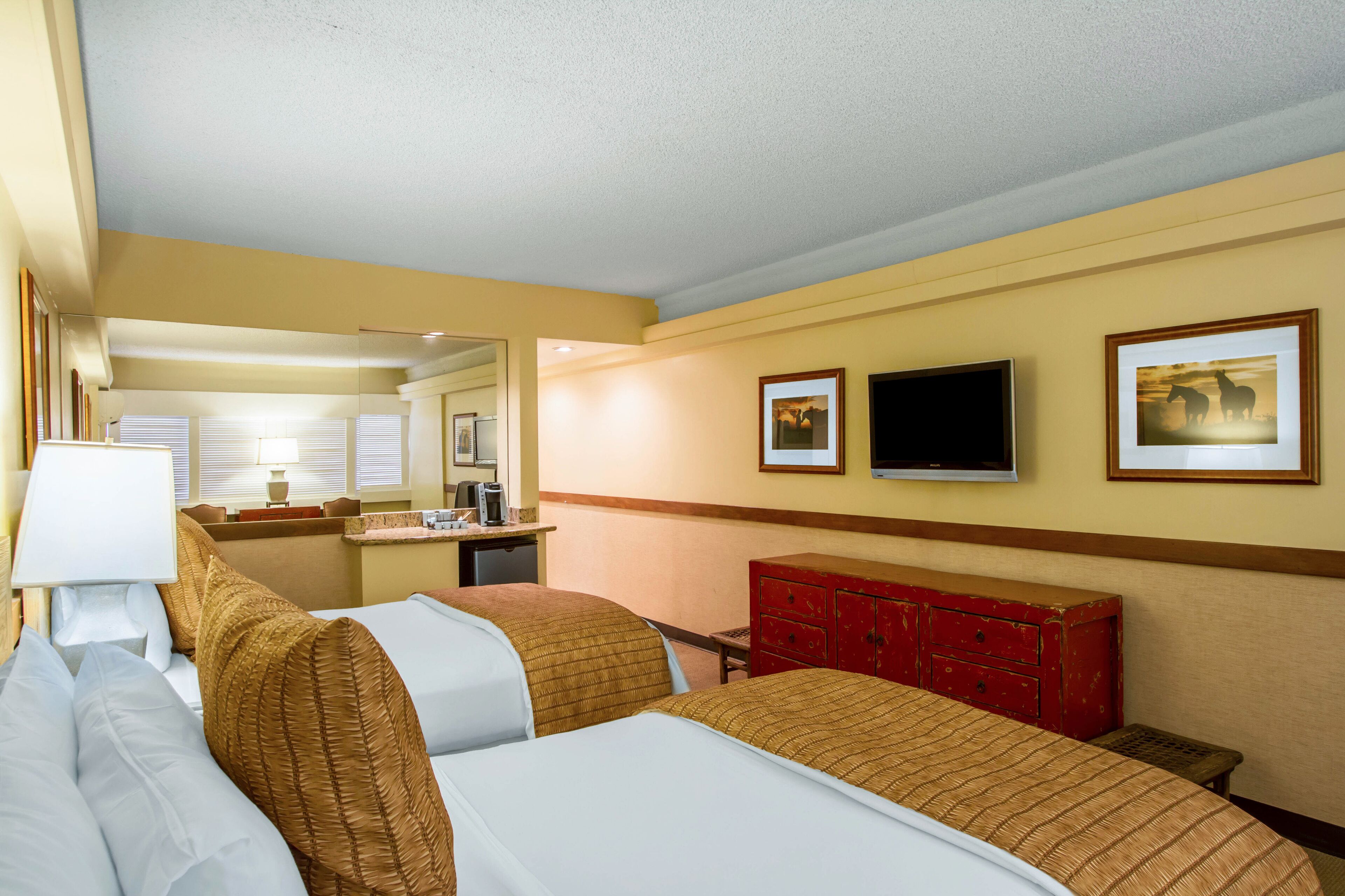Habitación de hotel con dos camas, un escritorio, un espejo y un televisor.