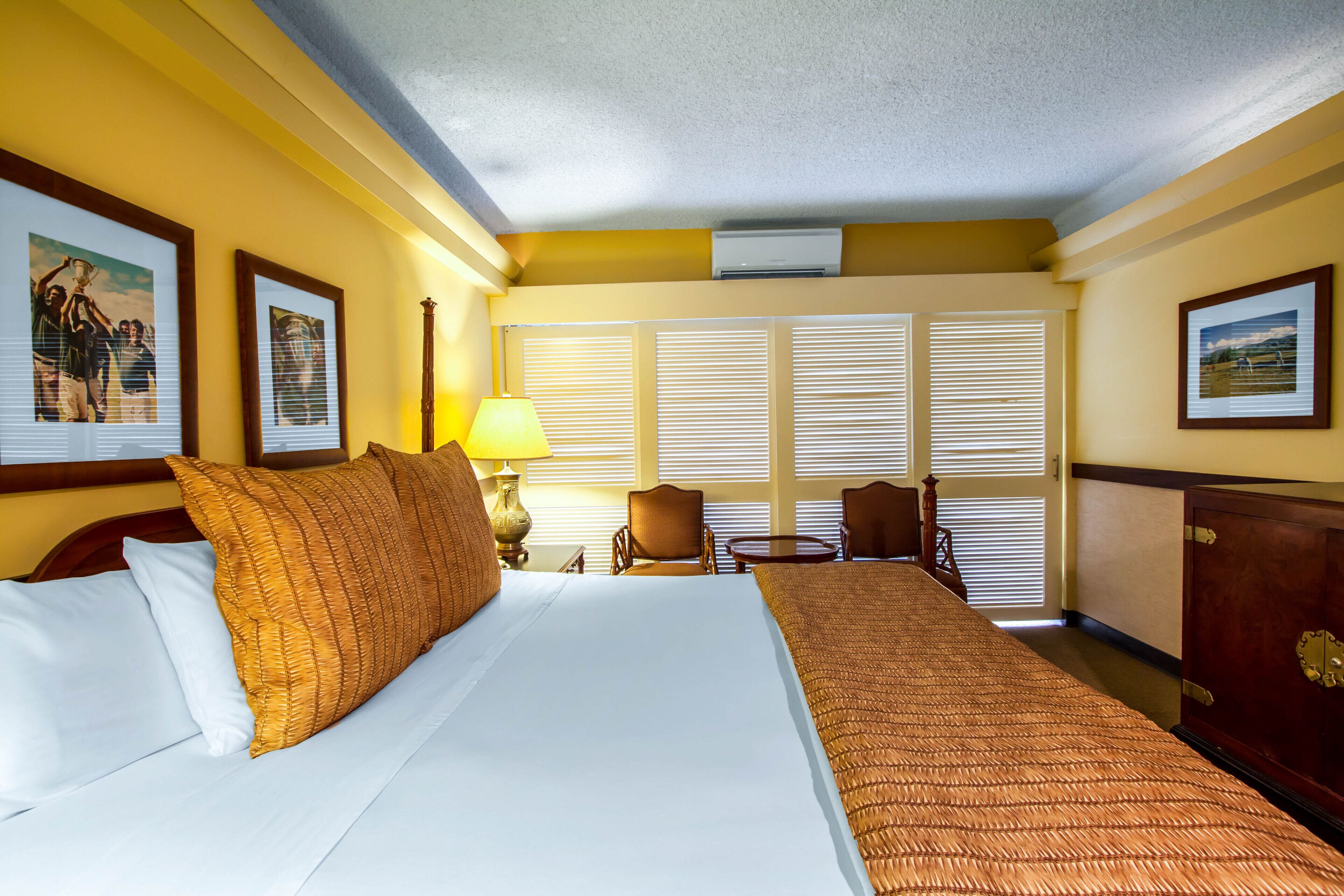 A hotel room with a large bed, a desk, two chairs, and a window with blinds.