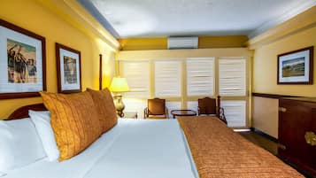 A hotel room with a large bed, a desk, two chairs, and a window with blinds.