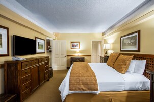 Quarto de hotel com uma cama grande, penteadeira de madeira, televisão de tela plana e quadros nas paredes.