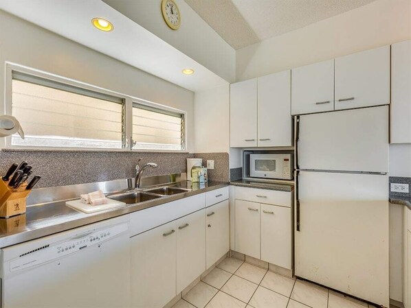A kitchen with white cabinets, a stainless steel sink, a microwave, and a refrigerator.