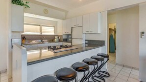 Een moderne keuken met witte kasten, een centraal eiland met krukken, en een raam voor natuurlijk licht.