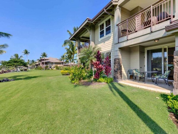 A two-story house with a balcony, a well-maintained lawn, and tropical plants. - High-Style 2 Bedroom – Halii Kai at Waikoloa 4C (WAIKOLOA)
