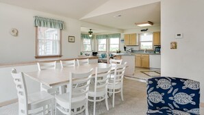 A dining area with a wooden table and white chairs, a kitchen in the background, and a patterned armchair. - My Happy Place: Private Pool & Hot Tub, Rec Room w/ Foosball and Air Hockey (Corolla)