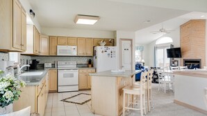 A modern kitchen with wooden cabinets, a central island, and a dining area with white chairs. - My Happy Place: Private Pool & Hot Tub, Rec Room w/ Foosball and Air Hockey (Corolla)