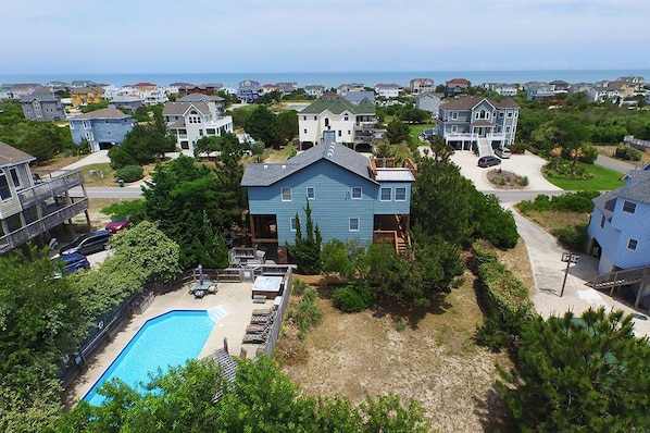 Un barrio residencial con una casa grande azul, una piscina y vista al océano.