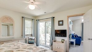 A bedroom with a bed, a ceiling fan, a television, a wicker dresser, a blue sofa, and a sliding glass door leading to a balcony. - My Happy Place: Private Pool & Hot Tub, Rec Room w/ Foosball and Air Hockey (Corolla)