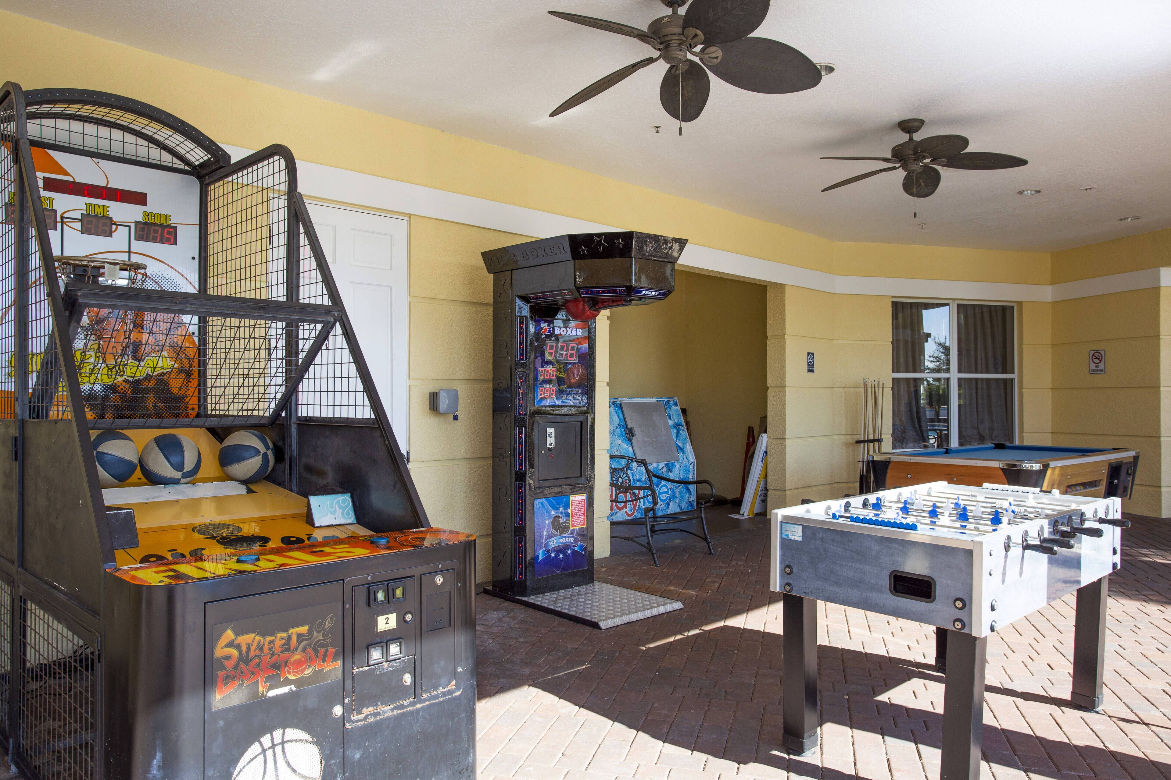 A room with a foosball table, a basketball arcade game, and a pool table.