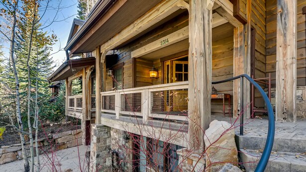 Een houten chalet met een stenen fundering, een balkon met een metalen hekwerk, en het cijfer '2354' op de muur.