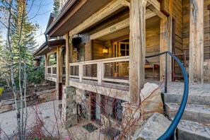 A wooden cabin with a stone foundation, a balcony with a metal railing, and a visible number '2354' on the wall.