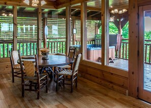 Relax in a cozy cabin with a dining area, round table, and four chairs, surrounded by large windows and a hot tub.