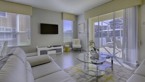 Een moderne woonkamer met een bank, een glazen salontafel, een televisie en een schuifpui naar een balkon.