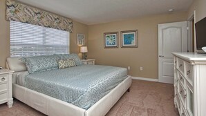 Un dormitorio con cama, mesitas de noche, cómoda y dos cuadros colgados en la pared.