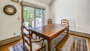 A dining area with a wooden table and chairs, a patterned rug, and a large window with curtains.