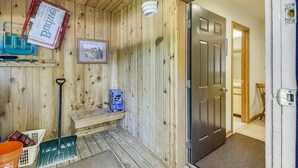 A wooden interior with a door, a bench, a broom, a bucket, and a trash bin.