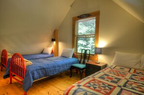 Une chambre avec deux lits, une fenêtre avec des stores, une chaise et une table de chevet avec une lampe.