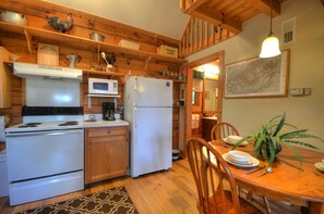 A compact kitchen with a stove, microwave, and refrigerator, wooden cabinets, and a dining table with chairs. - 2BR cabin in Bryson City with hot tub, fireplace, WiFi, and mountain views. Free train and rafting (Bryson City)