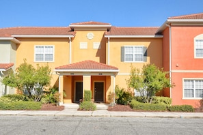 A row of townhouses with a red-tiled roof, a central entrance with a porch, and a small garden area in front.