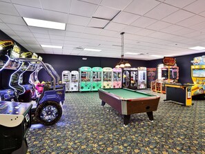 A room with a pool table, arcade games, and a car-shaped game.