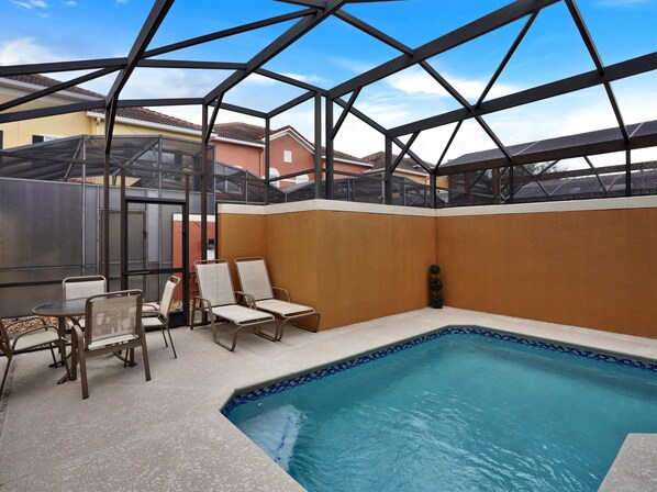 A pool area with chairs, a table, and a glass-enclosed structure.