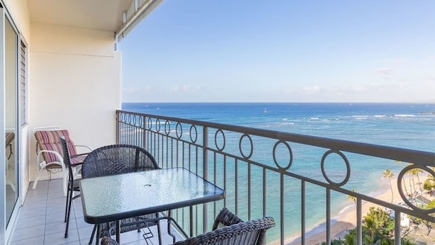 A balcony with a table and chairs, overlooking a beach and ocean. - Families Love the View and Fun Decor! Free WiFi, Full Kitchen–Waikīkī Shore #PH05 (HONOLULU)