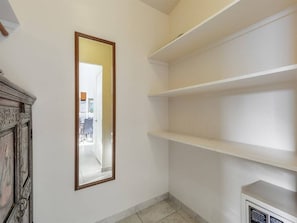 Ein Teil des Raumes zeigt eine weiße Wand, einen Spiegel und ein weißes Regal.