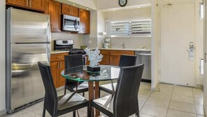 A modern kitchen with wooden cabinets, stainless steel appliances, and a glass dining table. - Families Love the View and Fun Decor! Free WiFi, Full Kitchen–Waikīkī Shore #PH05 (HONOLULU)