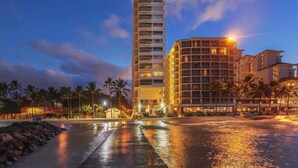 Et hotel ved stranden med en høj bygning og en lavere struktur, begge med flere etager og balkoner.