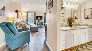 A modern living room with a blue sofa, a television, and a dining area with a kitchen counter and cabinets. - Cozy Lake Front Condo (Branson)