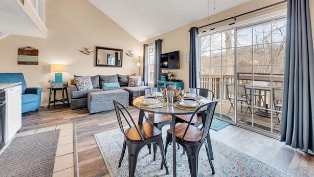A spacious living room with a dining area, a sofa, a TV, and a large window with curtains. - Cozy Lake Front Condo (Branson)