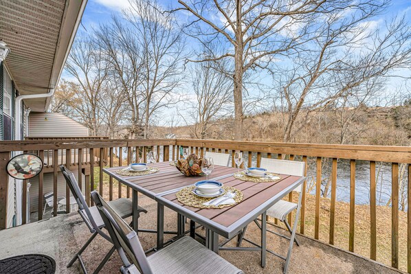 A wooden deck with a table set for two, overlooking a body of water and trees.