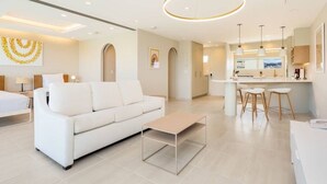 Una habitación de hotel moderna con un sofá blanco, una mesita de centro y una zona de cocina con taburetes de bar.
