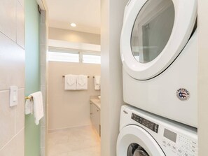 A laundry area with stacked washers and dryers, a visible control panel, and a towel rack with towels. - Modern Décor W/Private Lanai and A/C – Waikīkī Shore #1106 (HONOLULU)