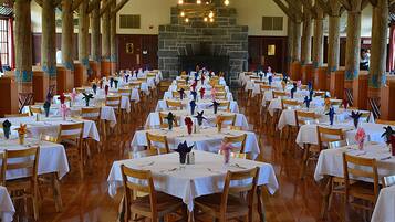 A large hall with rows of tables and chairs, a stone fireplace, and wooden beams.