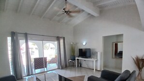 A spacious living room with a ceiling fan, a flat-screen TV on a white desk, and a large window with curtains. - Aruba private 3 bedroom holiday Villa, pool, walking distance to the beach (Noord)