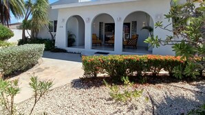 A modern building with three arched entryways, a gravel driveway, and a well-maintained garden with various plants and flowers. - Aruba private 3 bedroom holiday Villa, pool, walking distance to the beach (Noord)